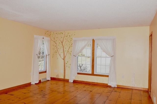 spare room featuring baseboards, visible vents, a textured ceiling, and wood-type flooring