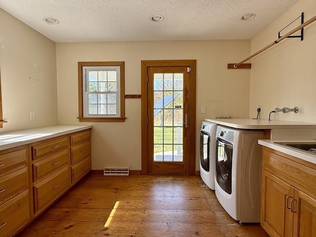 washroom with a textured ceiling, cabinet space, independent washer and dryer, and light wood-style floors