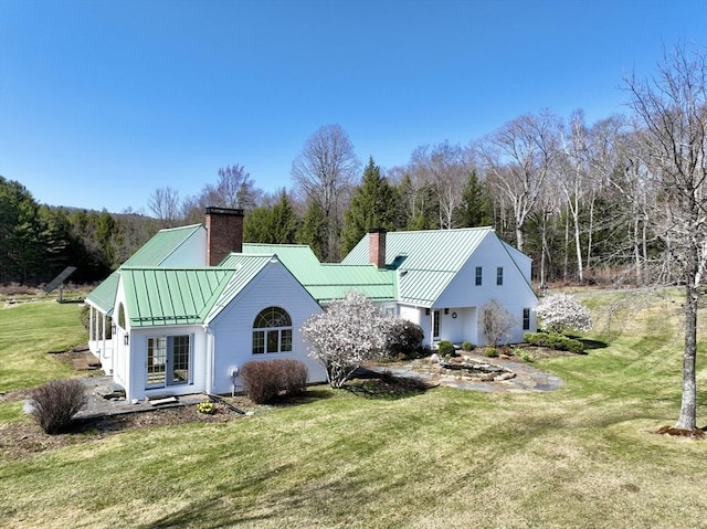 rear view of property with a chimney, a yard, a standing seam roof, and metal roof
