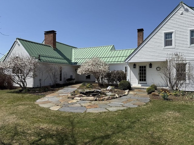 back of property featuring metal roof, a standing seam roof, a yard, and a chimney