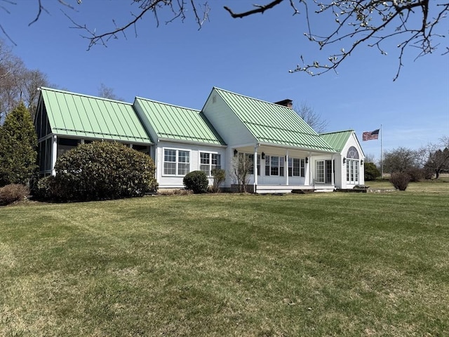 rear view of house featuring a chimney, a standing seam roof, metal roof, and a lawn