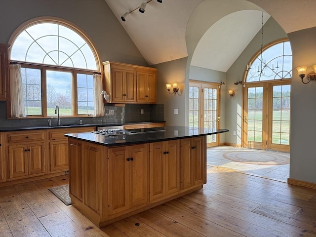 kitchen featuring a sink, decorative backsplash, light wood-type flooring, a kitchen island, and dark countertops