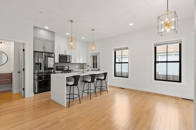 kitchen featuring a breakfast bar, an island with sink, a wealth of natural light, light wood-style flooring, and stainless steel appliances