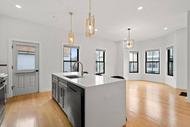 kitchen featuring light wood finished floors, dishwasher, an island with sink, light countertops, and a sink