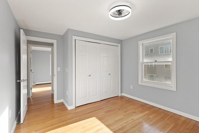 unfurnished bedroom featuring a closet, light hardwood / wood-style flooring, and a baseboard heating unit