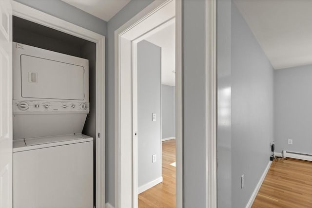 washroom featuring hardwood / wood-style floors, baseboard heating, and stacked washer and clothes dryer