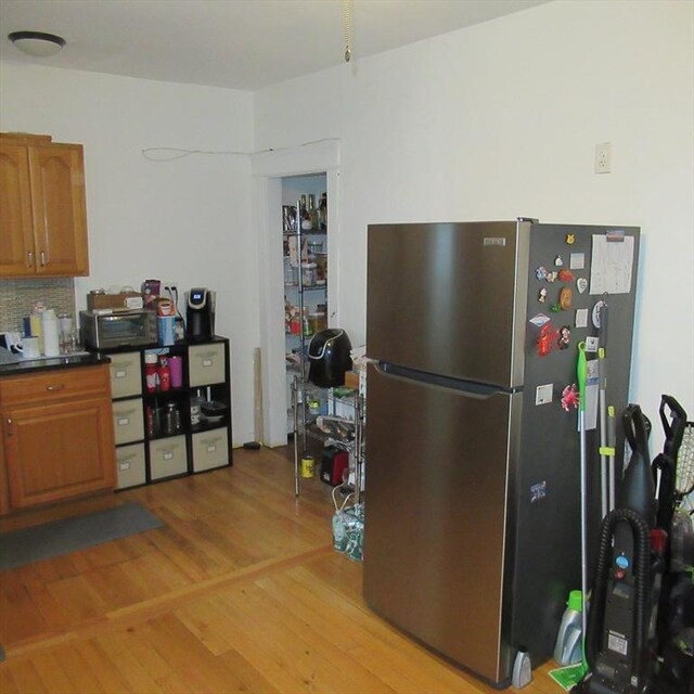 85-87 Belrose Ave, Lowell, MA 01852 - kitchen with freestanding refrigerator, brown cabinets, light wood finished floors, dark countertops, and decorative backsplash