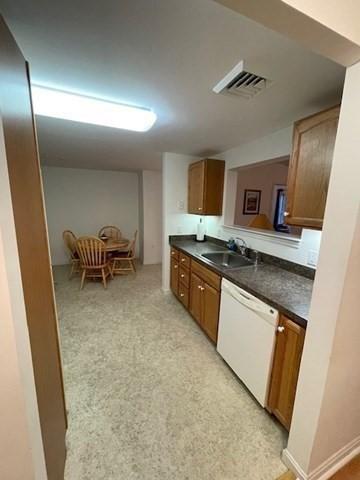 kitchen featuring white dishwasher, dark countertops, a sink, and brown cabinetry