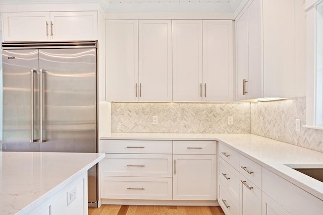 1 Wilsons Ln, Edgartown, MA 02539 - kitchen with white cabinets, built in fridge, decorative backsplash, light stone counters, and light wood finished floors