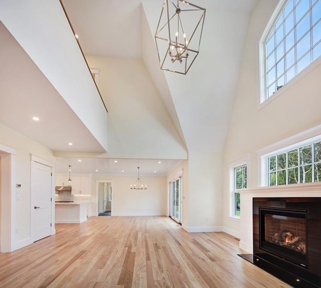 1 Wilsons Ln, Edgartown, MA 02539 - unfurnished living room featuring a chandelier, a high ceiling, a glass covered fireplace, light wood finished floors, and baseboards