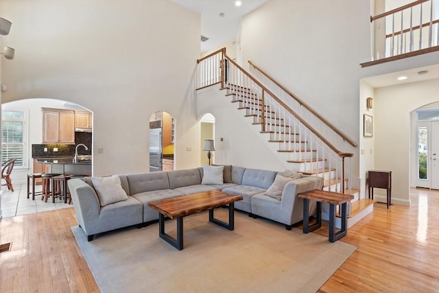 living room featuring arched walkways, recessed lighting, stairway, light wood-type flooring, and baseboards