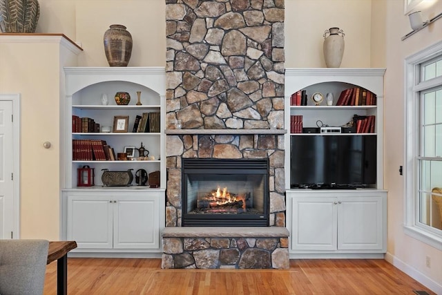 living area with built in features, a fireplace, light wood finished floors, visible vents, and baseboards