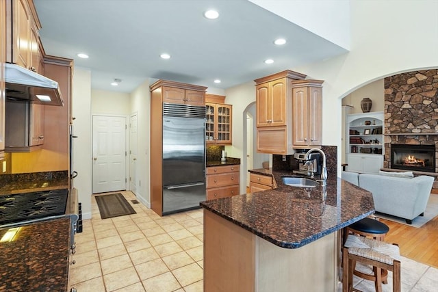 kitchen with stainless steel appliances, a sink, a peninsula, under cabinet range hood, and a kitchen bar