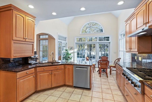 kitchen with light tile patterned floors, arched walkways, dark stone counters, appliances with stainless steel finishes, and a sink