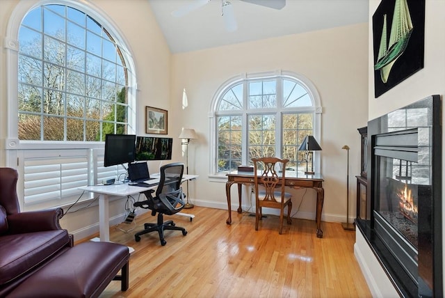 office space with ceiling fan, light wood-type flooring, a multi sided fireplace, and baseboards