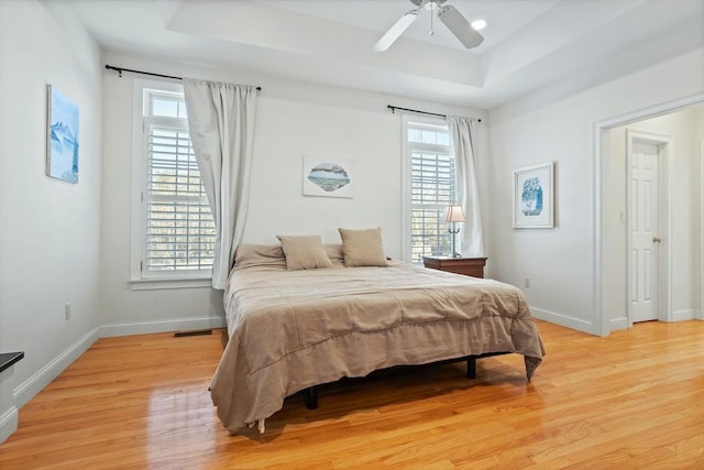 bedroom with light wood finished floors, baseboards, and a raised ceiling