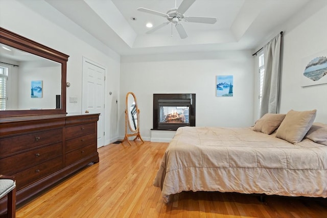 bedroom featuring a raised ceiling, light wood finished floors, multiple windows, and a multi sided fireplace