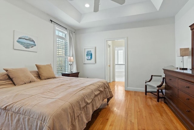 bedroom with a tray ceiling, light wood finished floors, recessed lighting, ensuite bath, and baseboards