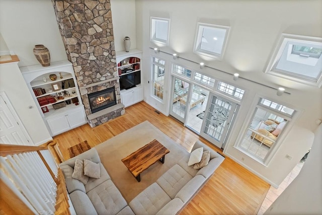 living area with built in features, light wood-type flooring, a fireplace, and a towering ceiling