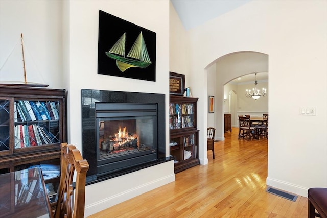 living area with arched walkways, wood finished floors, visible vents, baseboards, and a glass covered fireplace