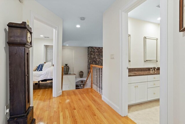 corridor featuring visible vents, a sink, light wood-style flooring, and an upstairs landing