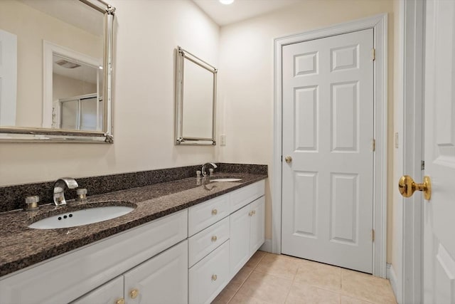 bathroom with double vanity, a shower with shower door, a sink, and tile patterned floors