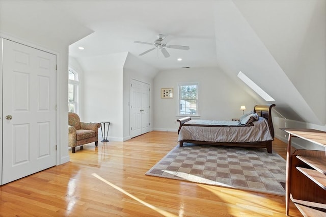 bedroom featuring vaulted ceiling with skylight, a ceiling fan, light wood-style flooring, and baseboards