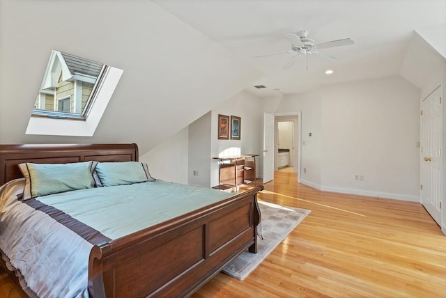 bedroom featuring light wood-style floors, vaulted ceiling with skylight, baseboards, and ceiling fan