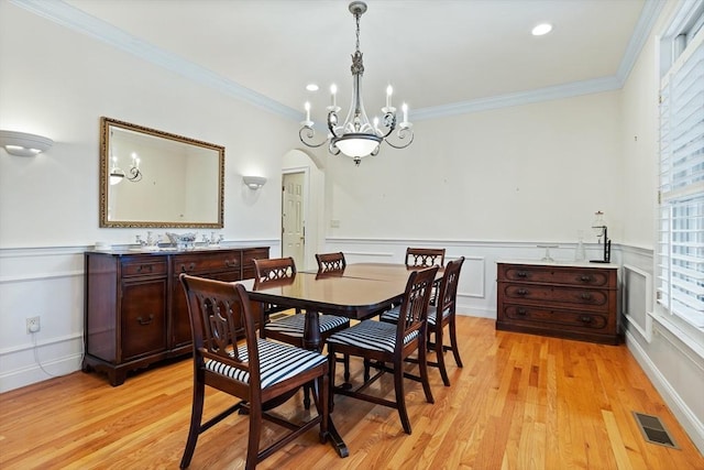 dining area with light wood-type flooring, arched walkways, visible vents, and crown molding