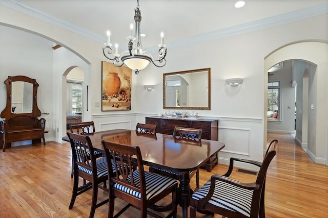 dining room with light wood-style flooring, arched walkways, and crown molding