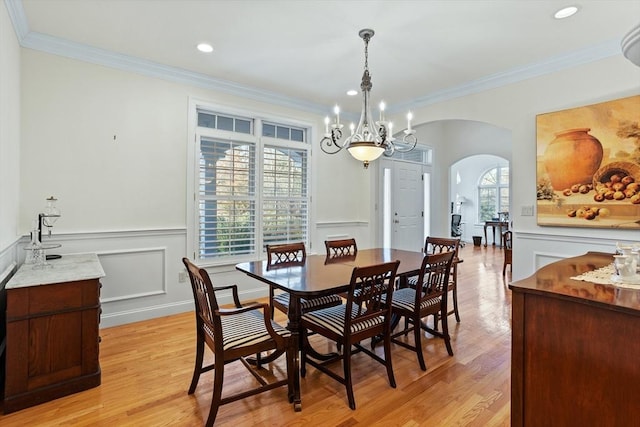 dining area featuring arched walkways, ornamental molding, light wood finished floors, and a decorative wall