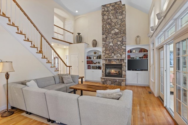 living area with stairs, high vaulted ceiling, a stone fireplace, and wood finished floors