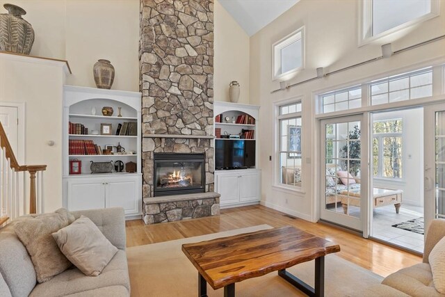 living room with high vaulted ceiling, stairway, a stone fireplace, and wood finished floors