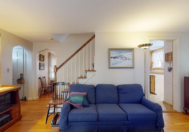 living area with light wood-style floors, stairway, and arched walkways