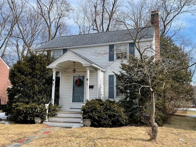 colonial-style house with a front lawn, a chimney, and a shingled roof