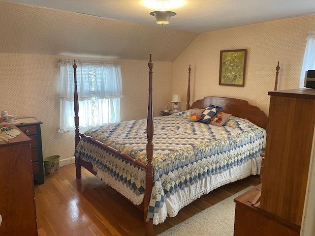 bedroom featuring lofted ceiling, wallpapered walls, baseboards, and wood finished floors