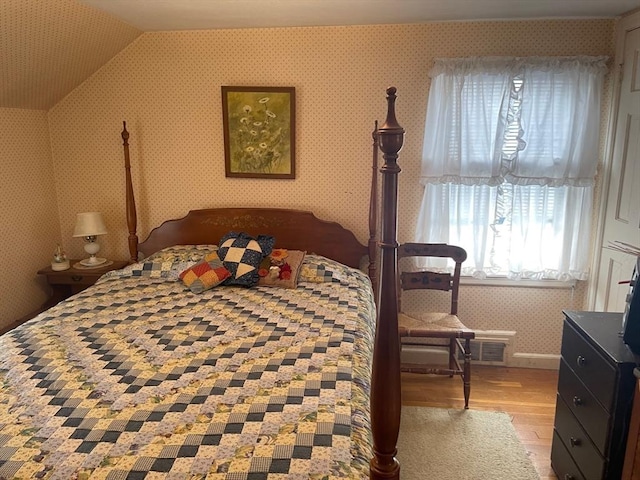 bedroom featuring wallpapered walls, visible vents, vaulted ceiling, and wood finished floors