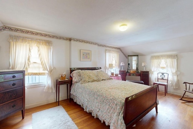 bedroom with vaulted ceiling, light wood-style flooring, and baseboards