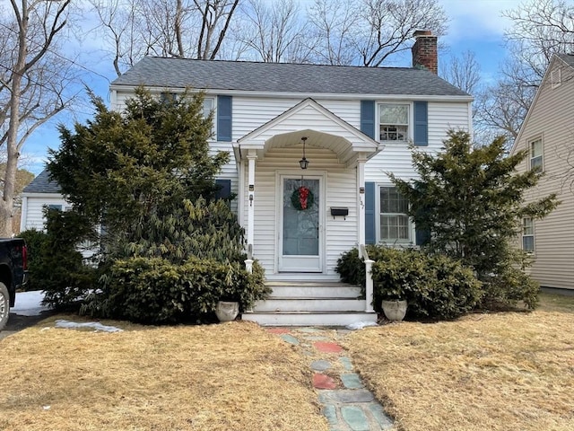 view of front facade with a front yard, roof with shingles, and a chimney