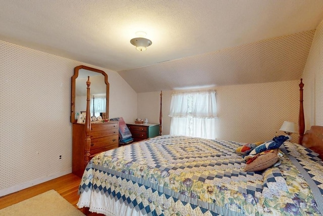 bedroom with a textured ceiling, wood finished floors, baseboards, vaulted ceiling, and wallpapered walls