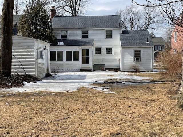 rear view of property featuring a shingled roof, an outdoor structure, and a chimney