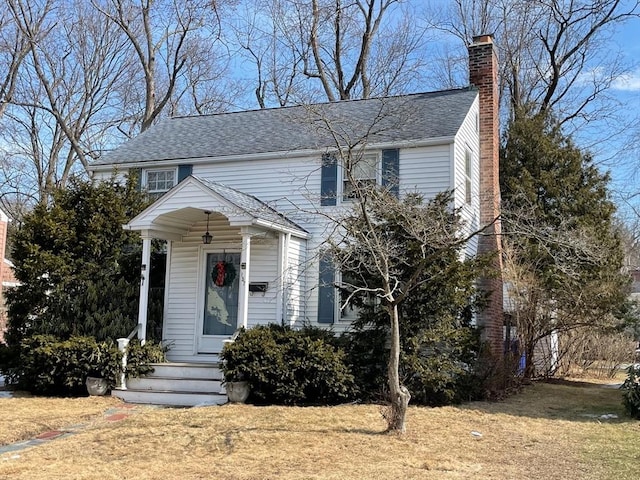 view of front of property featuring a chimney, a front lawn, and roof with shingles