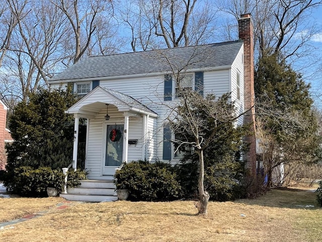 view of front of house with roof with shingles, a front lawn, and a chimney