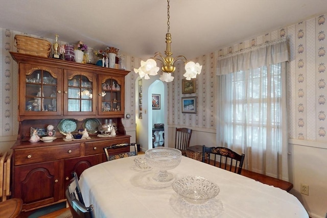 dining space featuring wallpapered walls, radiator heating unit, arched walkways, and a chandelier