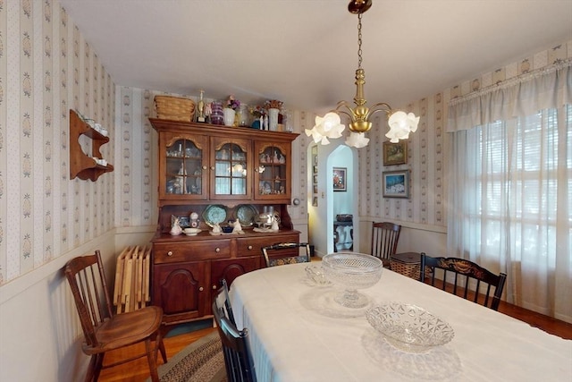 dining room featuring arched walkways, a wainscoted wall, radiator heating unit, a chandelier, and wallpapered walls