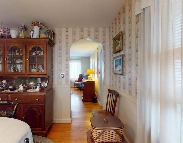 interior space with wallpapered walls, baseboards, arched walkways, and light wood finished floors