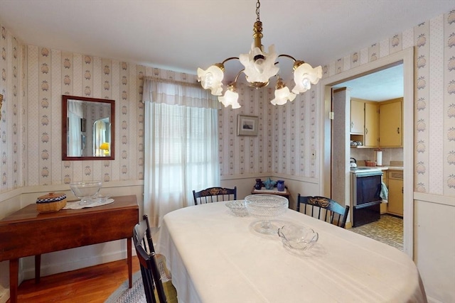 dining room with light wood-type flooring, wainscoting, an inviting chandelier, and wallpapered walls