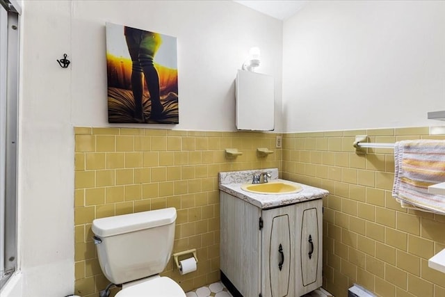 bathroom featuring tile walls, wainscoting, toilet, and vanity