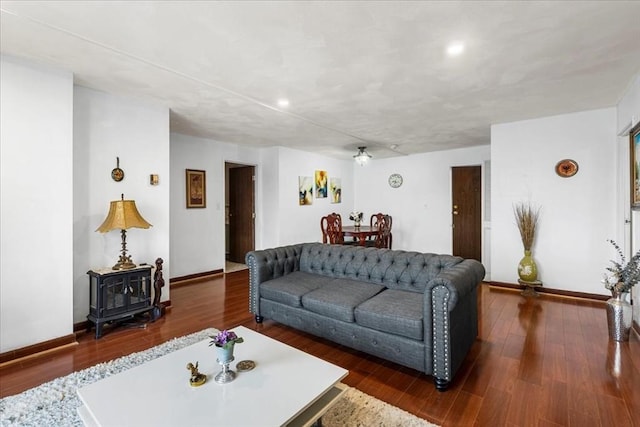 living room featuring a wood stove, baseboards, wood finished floors, and recessed lighting