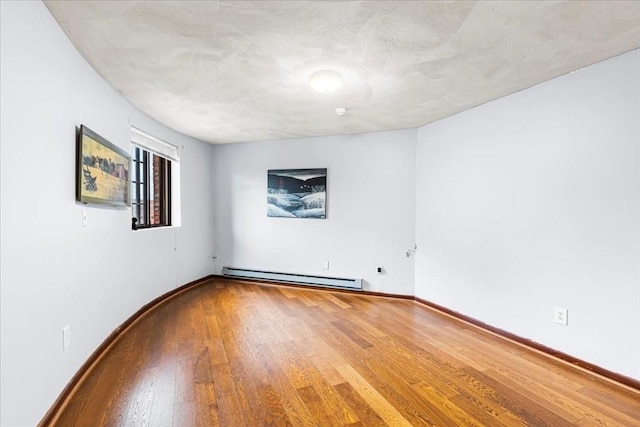 unfurnished room with a baseboard heating unit, wood finished floors, and baseboards
